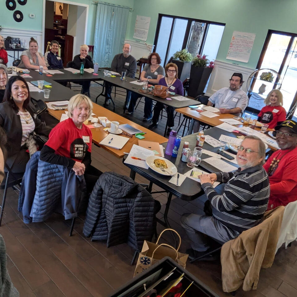 image of people sitting around a table in a circle looking at the camera and smiling